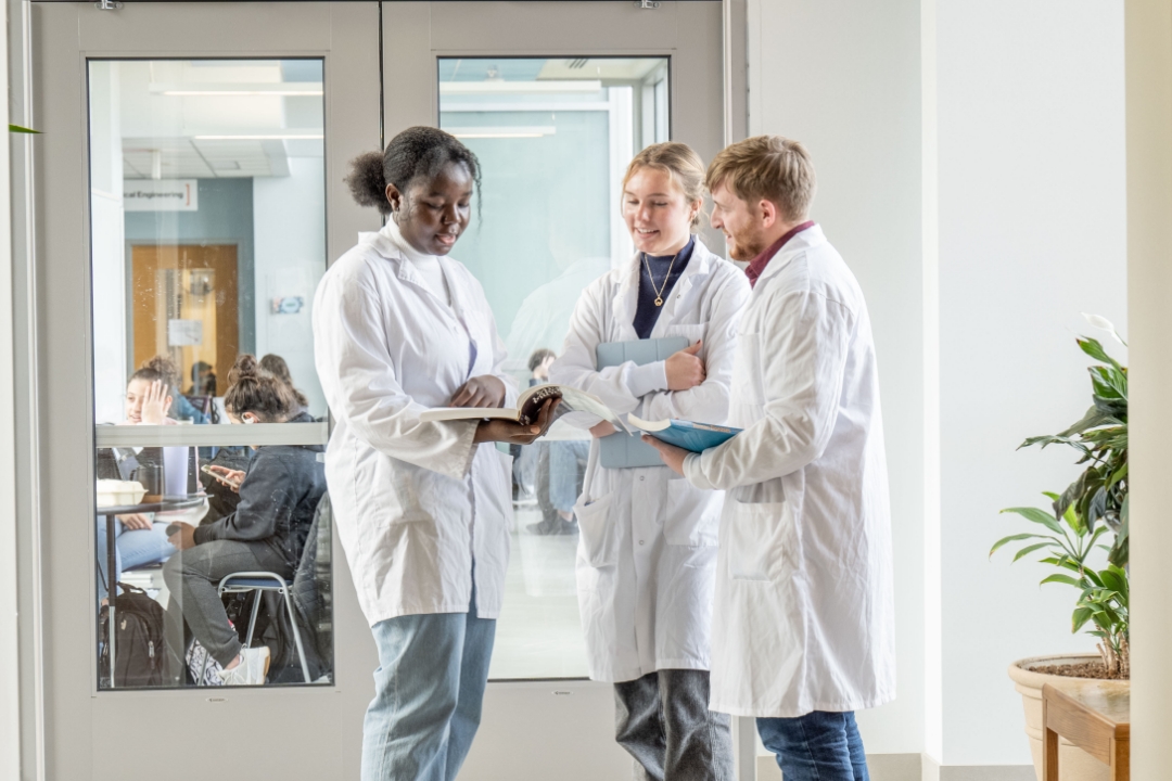 three people standing and talking to each other in a hallway wearing lab coats