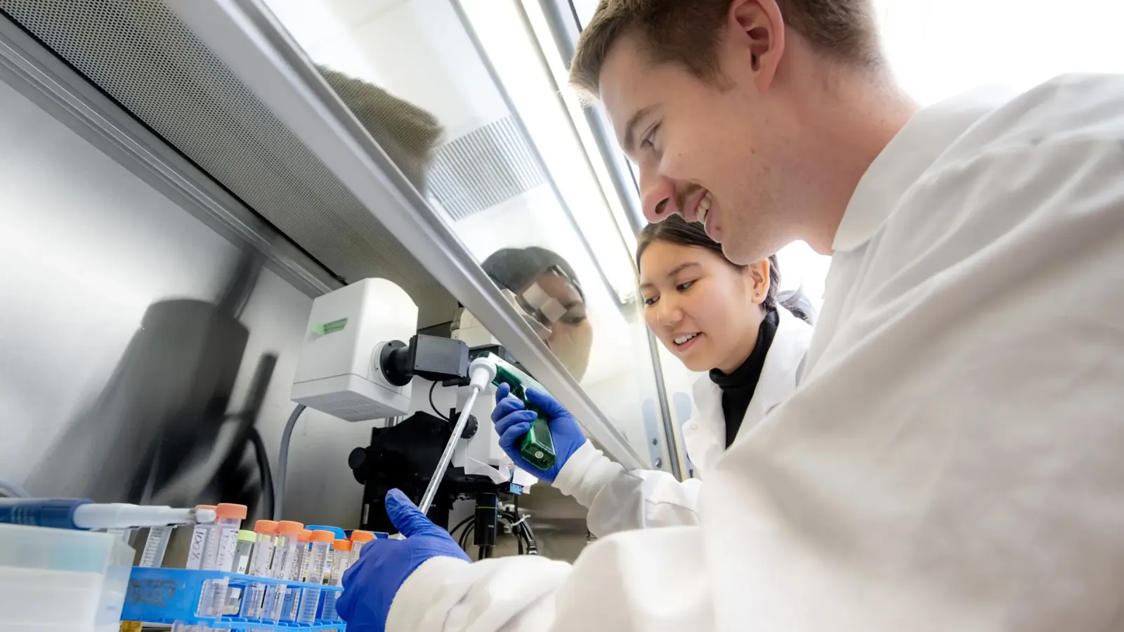 Two students in lab coats putting samples in vials.