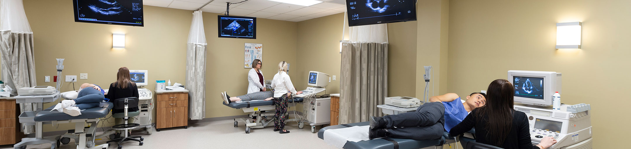 a hospital room with 3 patients all using ultrasound scanners with TVs on the wall showing the scan imagery