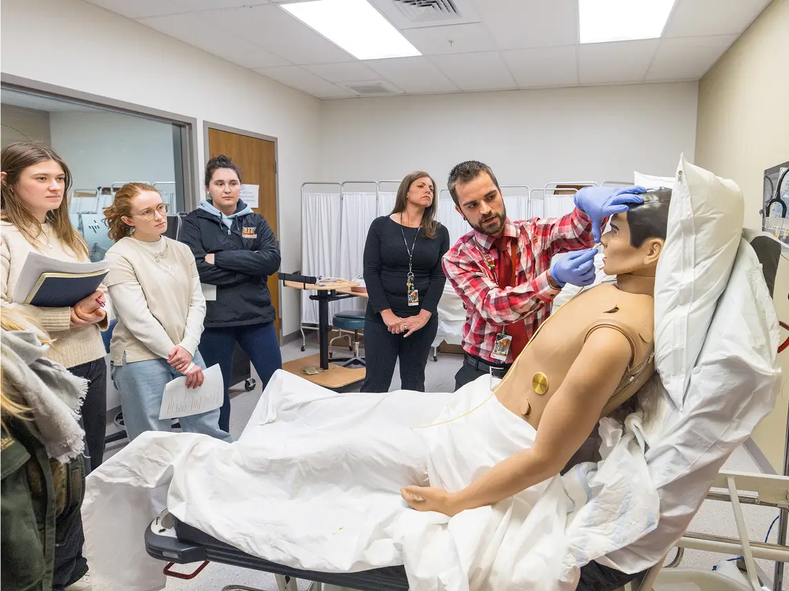 Students watch as an instructor performs a nose swab on a medical manikin.