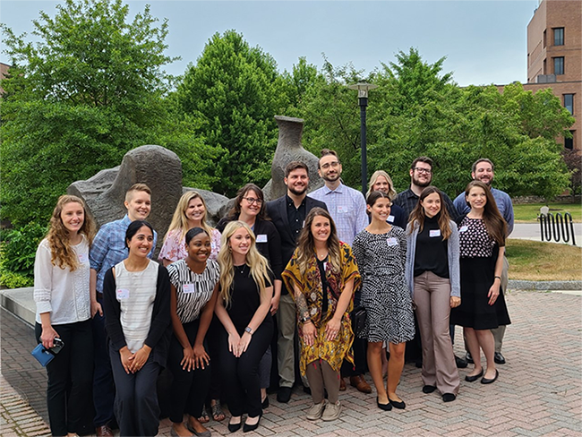 Group of 16 interns standing in front of sculpture on RIT campus