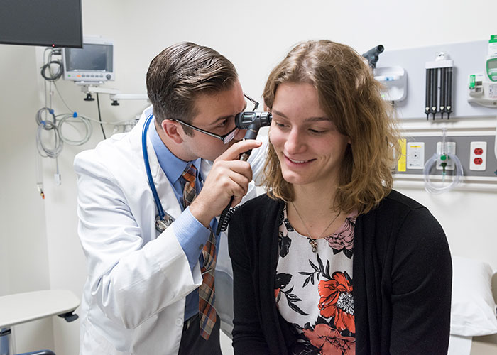 a women being examined by a male doctor using an otoscope