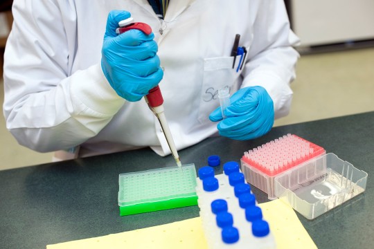 a person in a lab coat uses a pipette in a lab