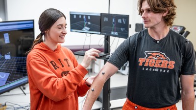 A female student placing sensors on a male students arm, waist, and neck.