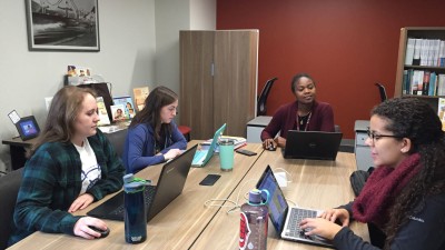 Three students and a faculty member working on laptops around a table.