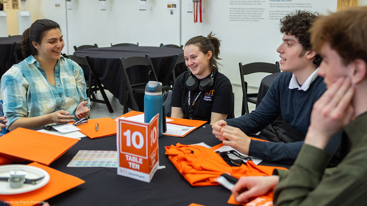 A group of students sitting at a table during an RIT Honors Program orientation, engaged in discussion and smiling.