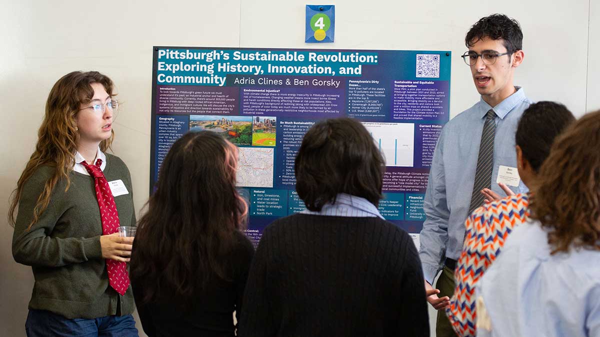 A student presents a research poster on Pittsburgh’s sustainable revolution to a small group at an academic symposium.