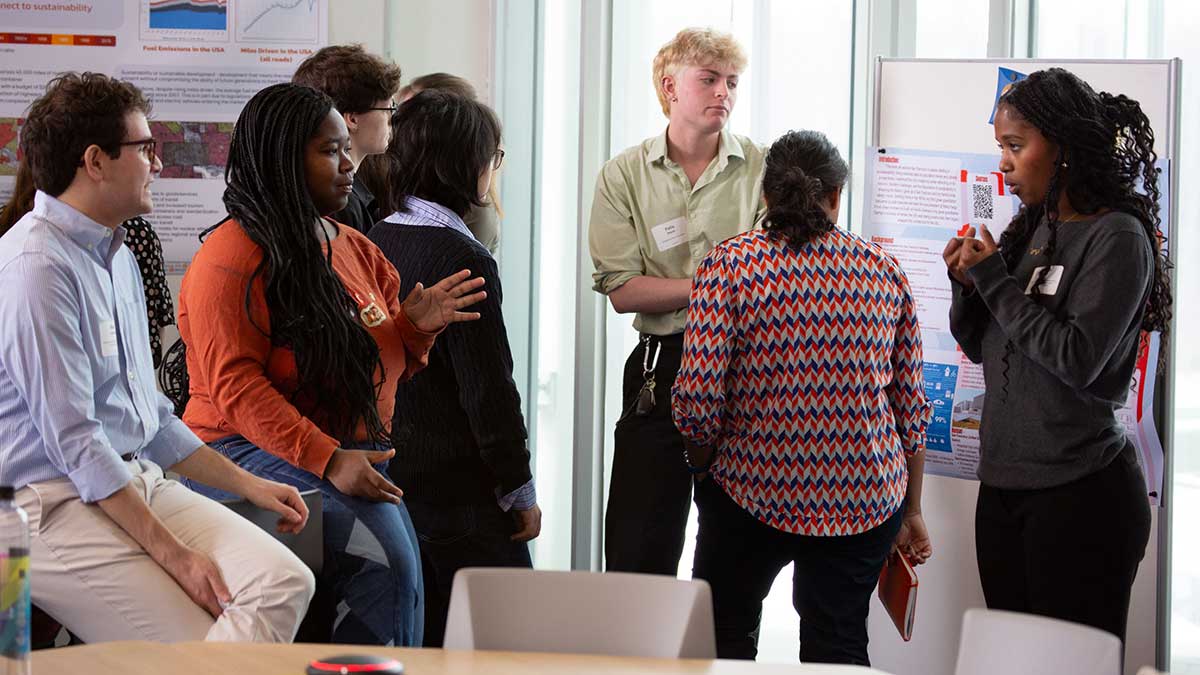 A student presents a research poster to a group of attendees during an academic symposium at RIT.