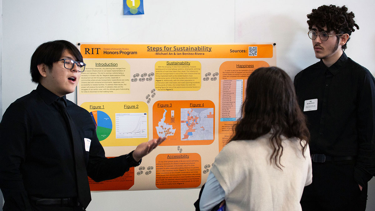 Two students explain a research poster titled 'Steps for Sustainability' to an attendee at an RIT Honors Program symposium.