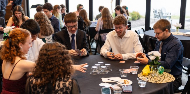 honors students dressed up nice at the honors gala, sitting around a circular black table, playing card games.