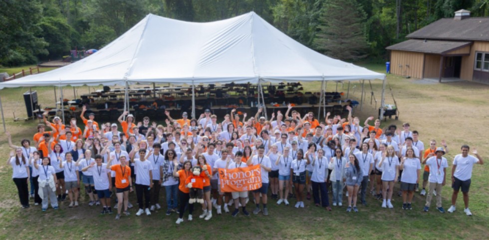 Roughly 100 honors students in a big group waving at camera