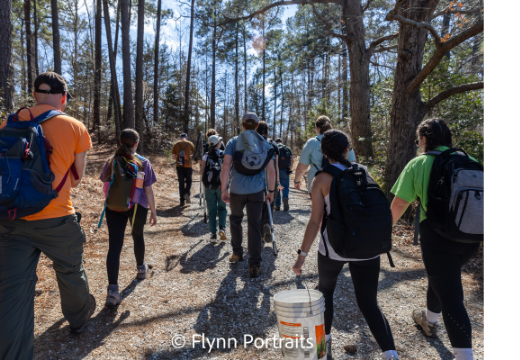 A group of people walking in a forest with backpacks and other tools