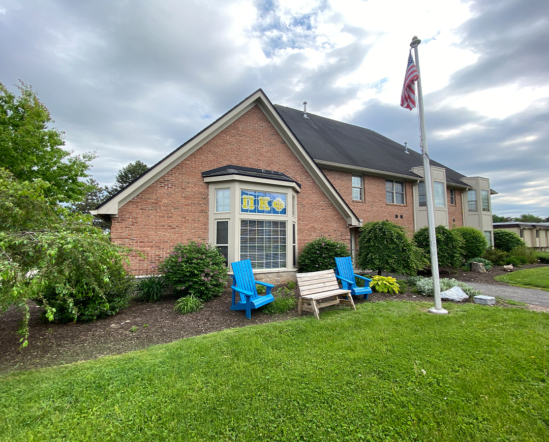 exterior of Greek Circle brick residence with a flag pole and Adirondack chairs outside