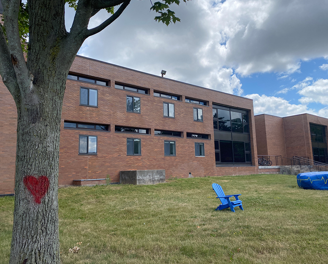 exterior of brick residence hall C with a chair and painted rock on lawn. Also showing a tree with a red heart drawn on it