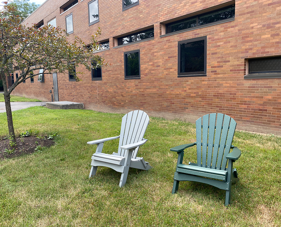 two adirondack chairs placed outside brick residence hall
