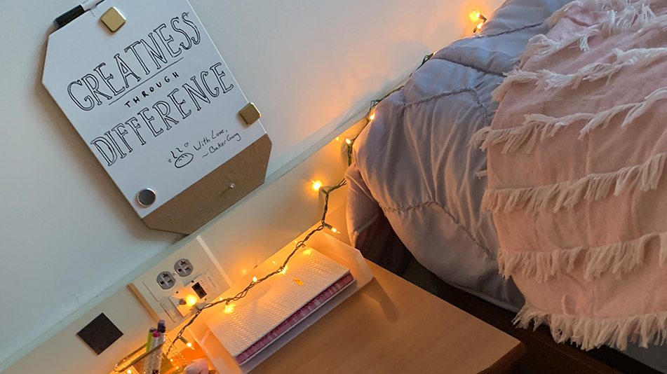 a desk at the end up a bed with a sign saying "Greatness through difference"
