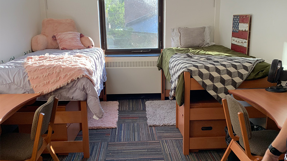 two twin beds with comforters next to a window and two desks