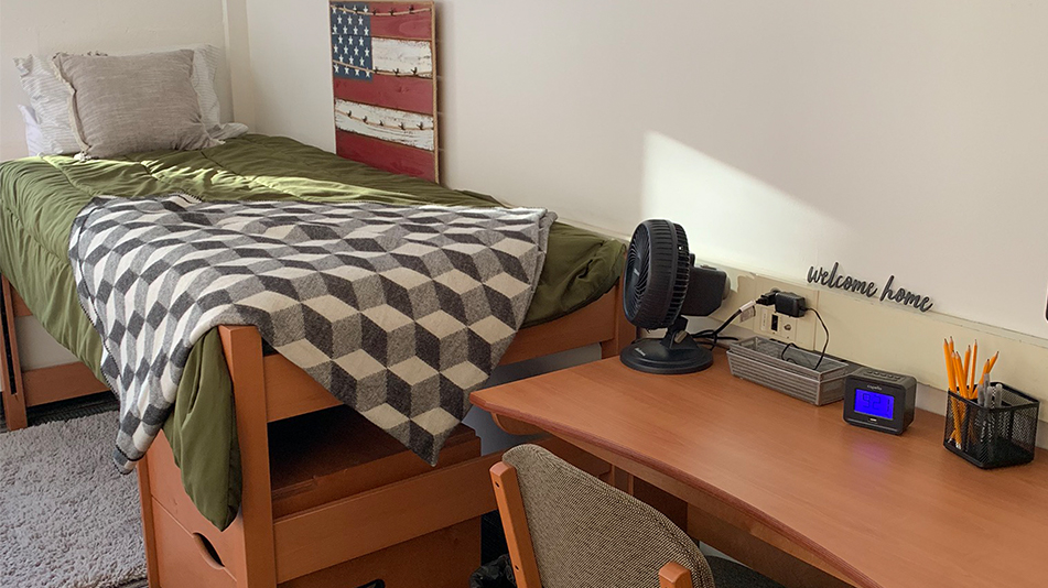 a bed with a green comforter next to a desk