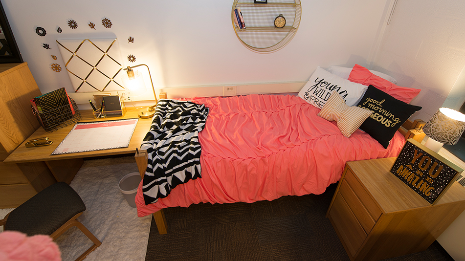 pink comforter on a bed next to a desk