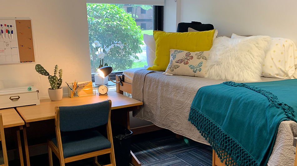 twin bed with a blue comforter with pillows, desk, and chair