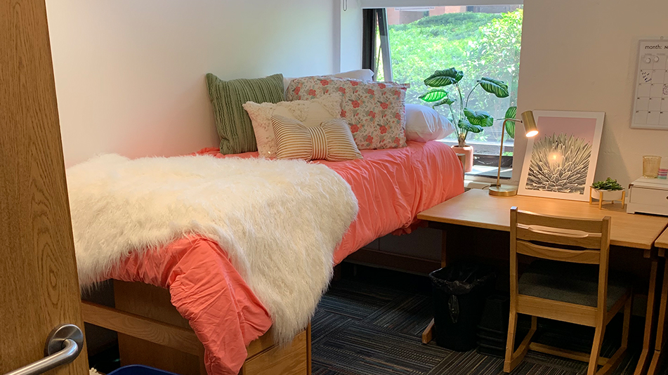 twin bed with a pink comforter with pillows, desk, and chair