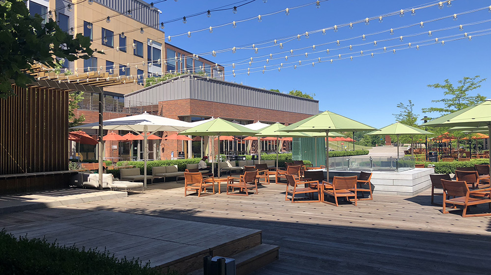 plaza with wood stage, tables and umbrellas, and a fire pit