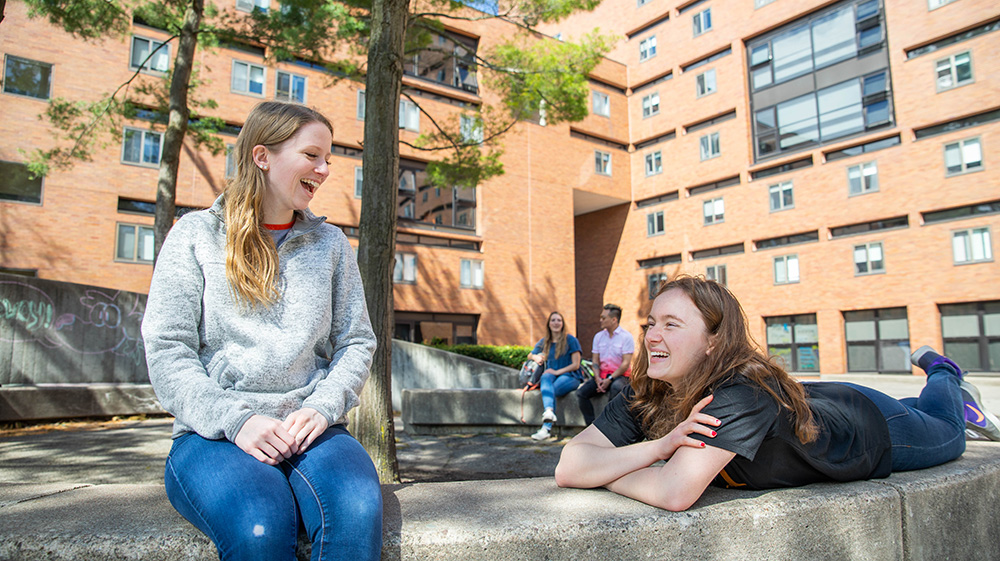 four people sit outdoors in a quad talking