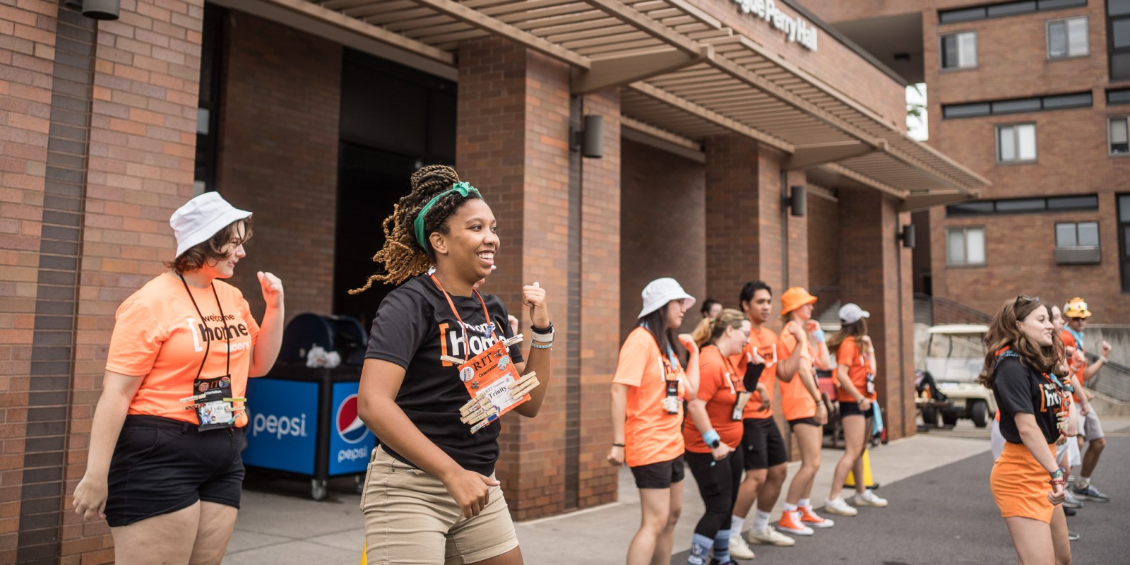 Student orientation workers outside of the residence hall dancing in a line with orange and black shirts that say welcome home tigers