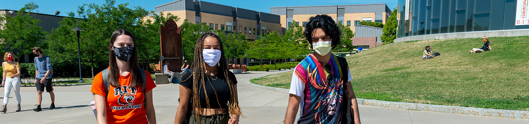 three students walk near Fountain Park on the RIT campus wearing masks
