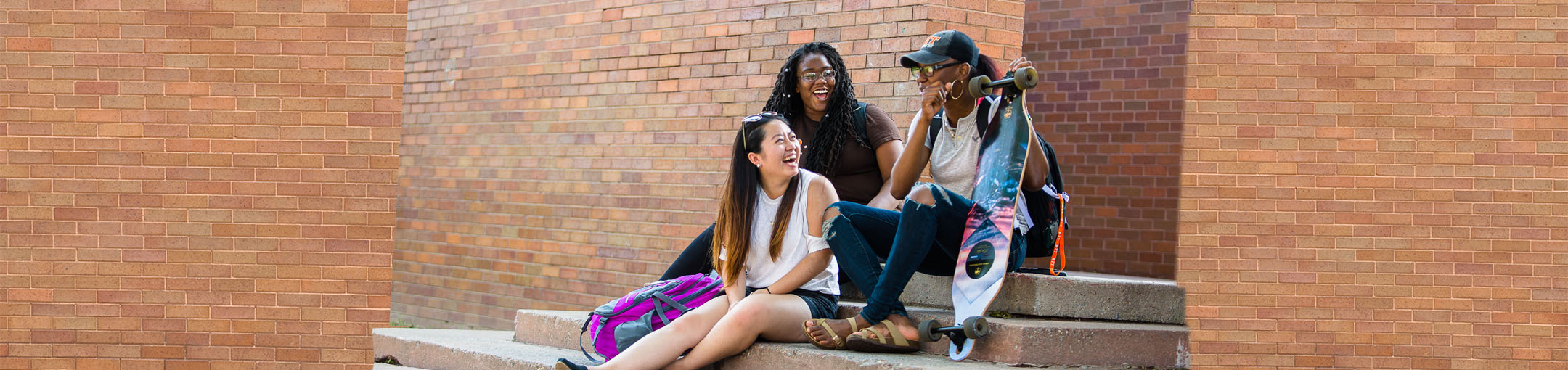 students sit on steps in front of a brick building