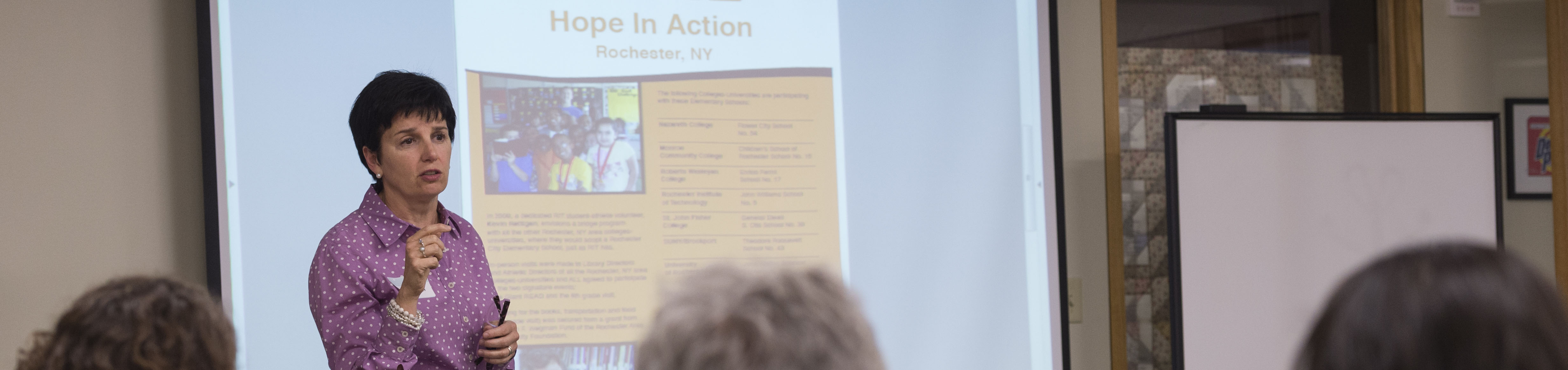 a person speaks to a group in front of a projection screen