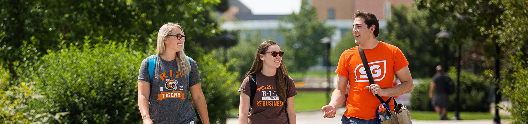 3 students walking next to each other wearing orange and brown shirts