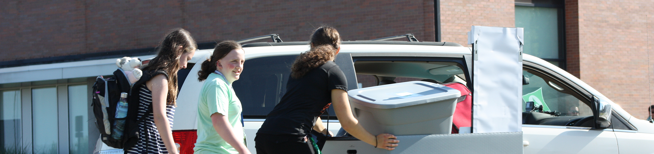 3 students walking next to each other with packed bags and a moving cart