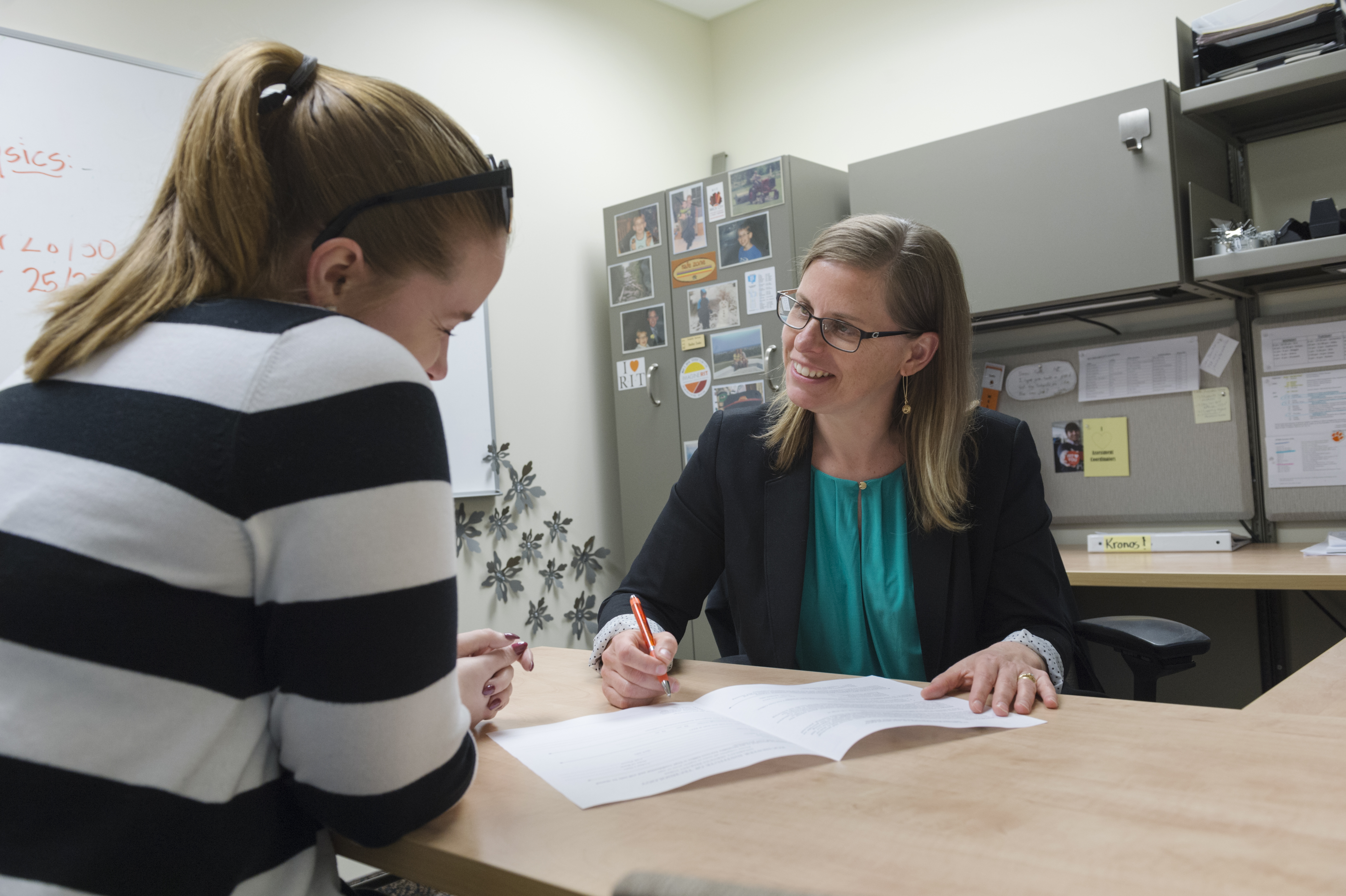 student at a desk talkinhg to a woman in a green shirt