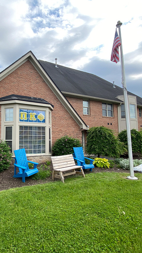 front of a two story brick house with blue adirondack chairs and a flag pole in front