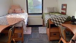 two twin beds with comforters next to a window and two desks