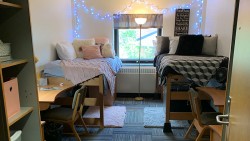 two twin beds with comforters next to a window. two desks and a closet shown