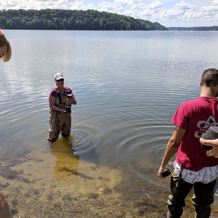 four researchers collecting sediment samples from a lake.