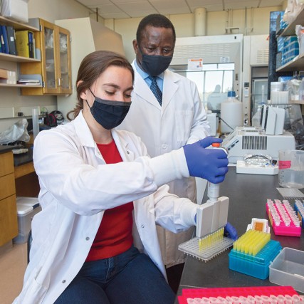 student using pipette as researcher looks on.