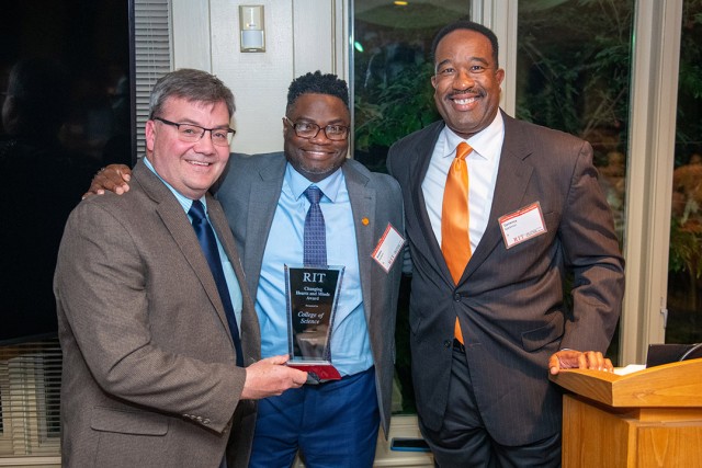 three college staff members posing with a glass award.