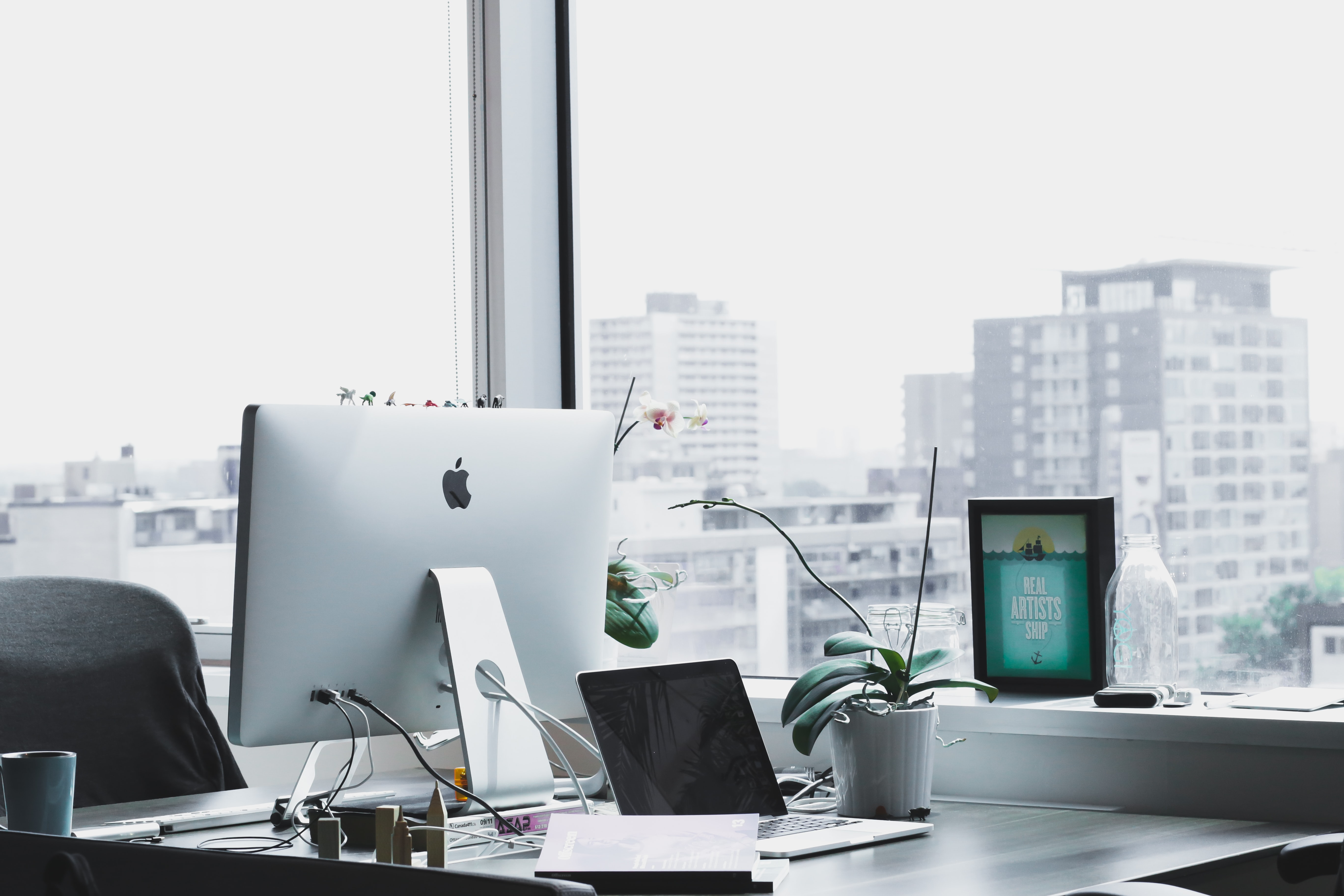 brightly lit office with computer and desk and large window overlooking a city