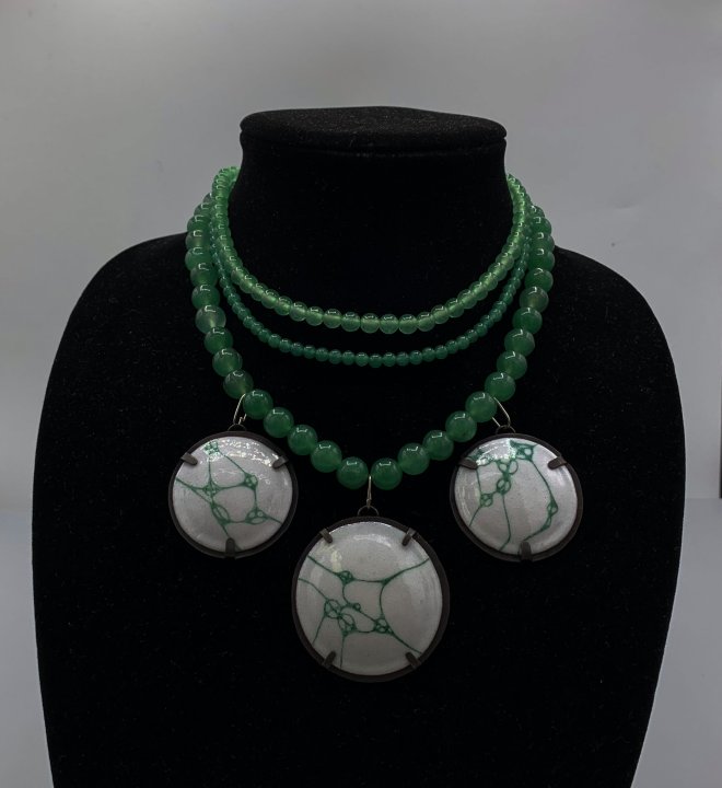 Necklace strung with adventurine beads and enamel pendants, painted with green web-like designs.