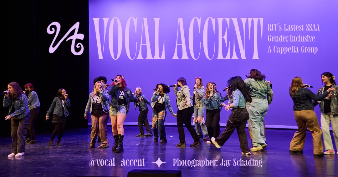 Vocal Accent, a diverse SSAA Acapella Group, performing onstage wearing their signature attire: denim jackets, whilst holding mics in their hand.