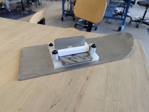 A side-angle view of the ski with a metal plate and a white mounting bracket. The bracket features a small, upright metal plate, for attachment purposes. The ski is 4.5 inches wide and 12 inches long.