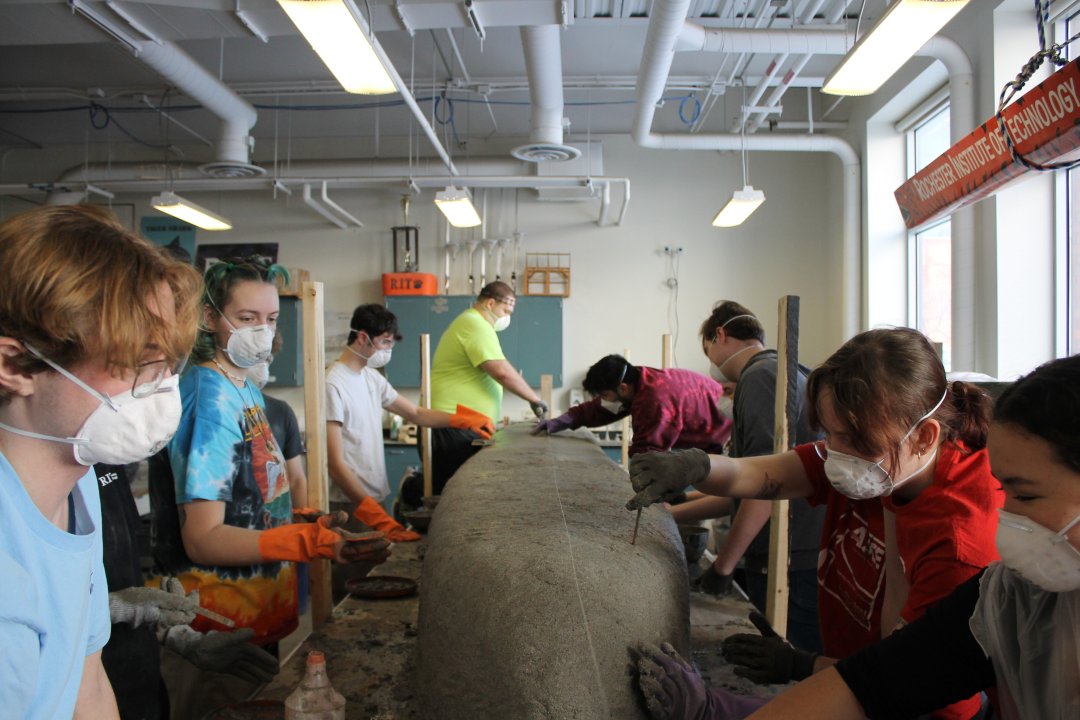 People gathered around the concrete canoe checking depth and placing concrete.