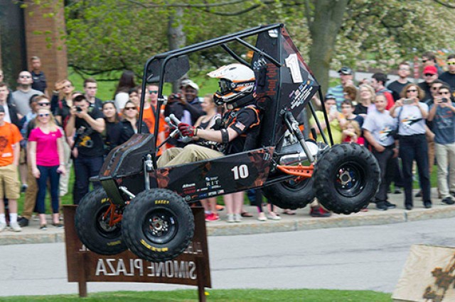 A student drives the Baja Racing vehicle as the crowd looks on. The car sails through the air after driving over a ramp.