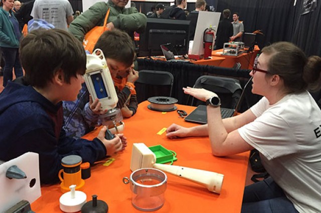 Cayla Denning sits at a table and demonstrates the prototype device for three young boys.