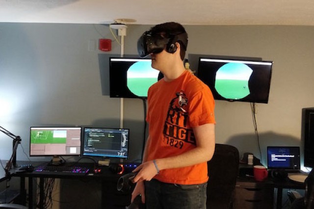 Student wearing a virtual reality headset standing in front of computer monitors.