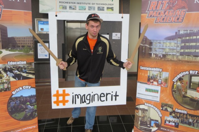 Chad Krohn poses with two cardboard swords inside of a cardboard polaroid cut-out used for photo-ops.