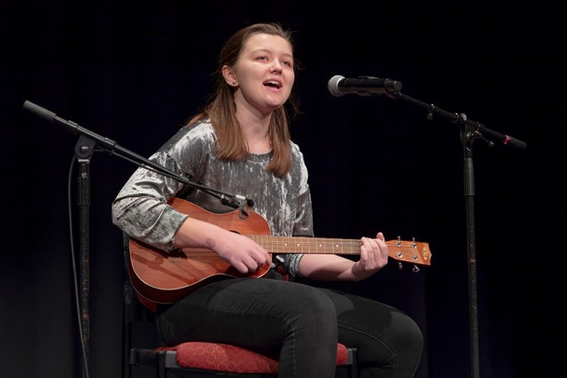 student playing guitar and singing into microphone.